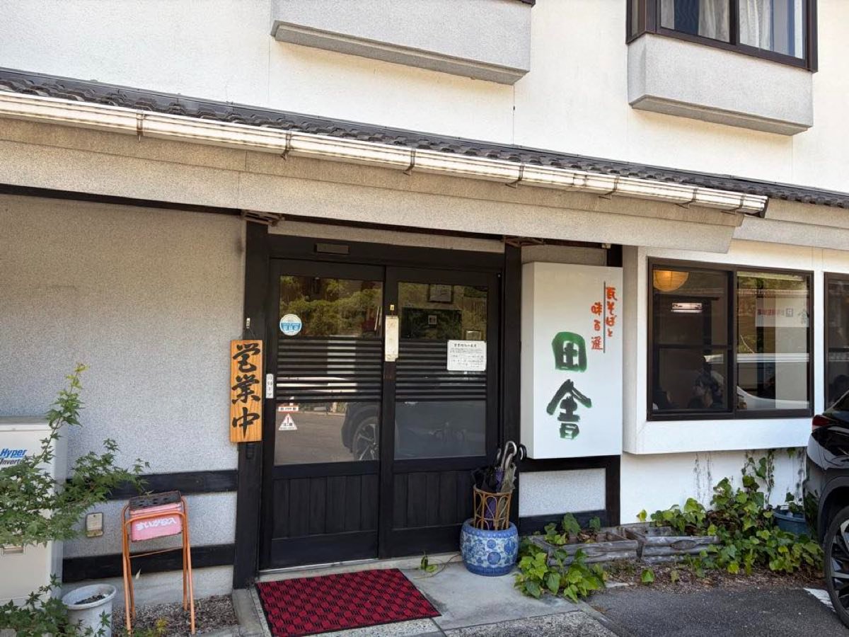 瓦そば田舎の外観。白壁に「瓦そばと味百選 田舎」の看板と営業中の木札